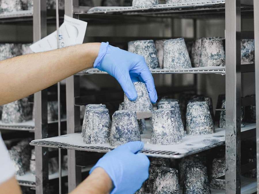 Gloved hands sliding a tray of stock onto stainless racking inside a chilled room