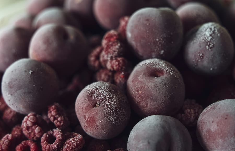 Frozen plums and raspberries furred with frost in a freezer room