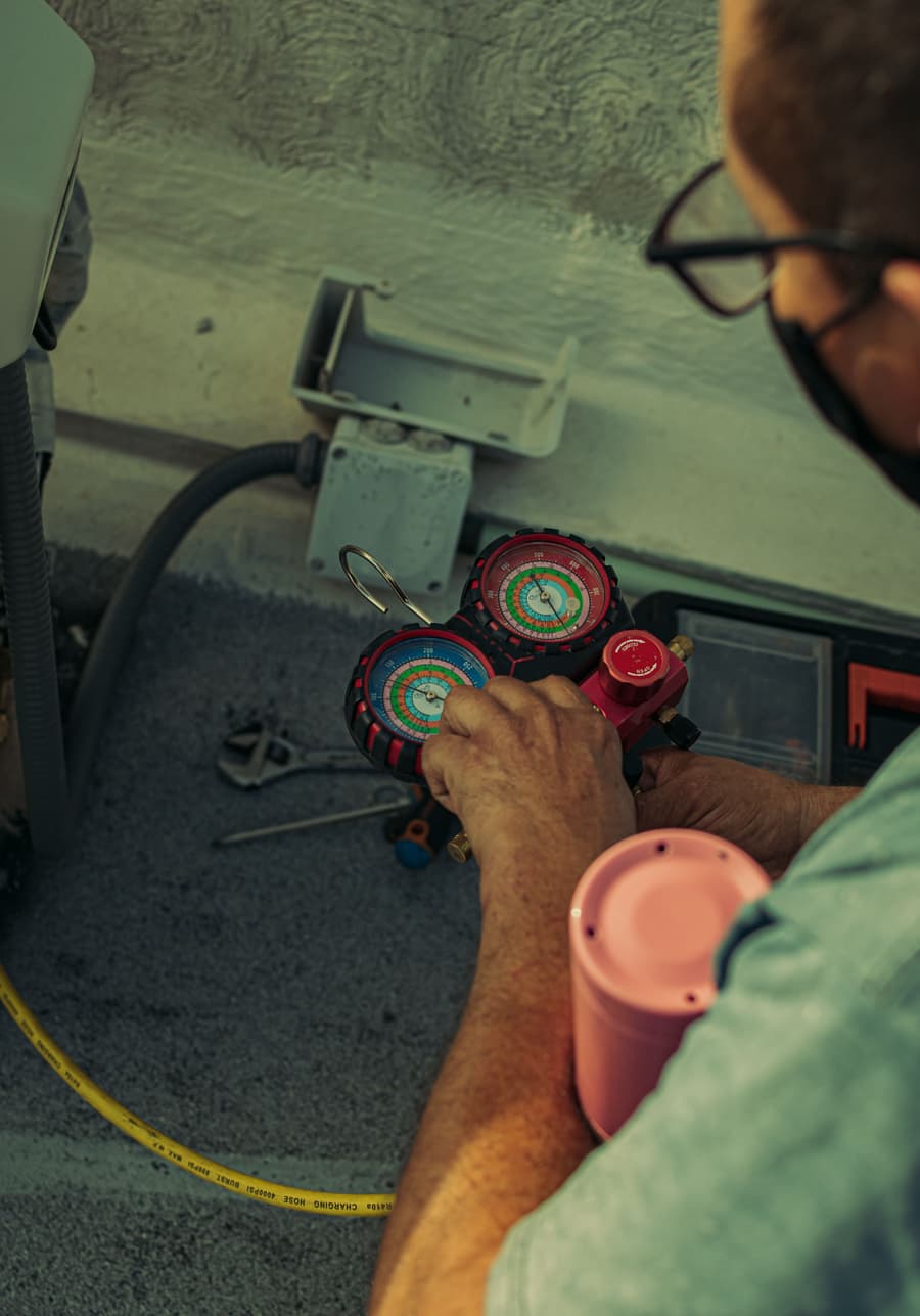 Technician's hands reading refrigerant manifold gauges on an outdoor unit