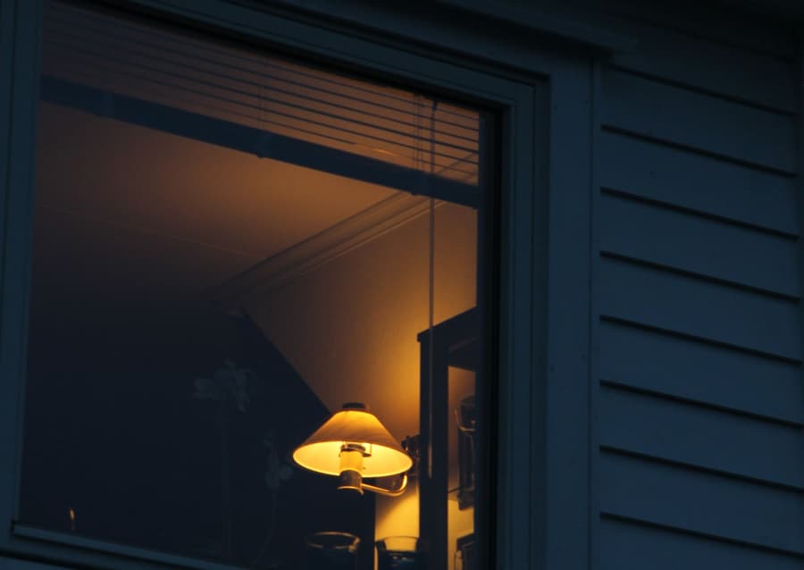 Lamp glowing in the window of a weatherboard house at night