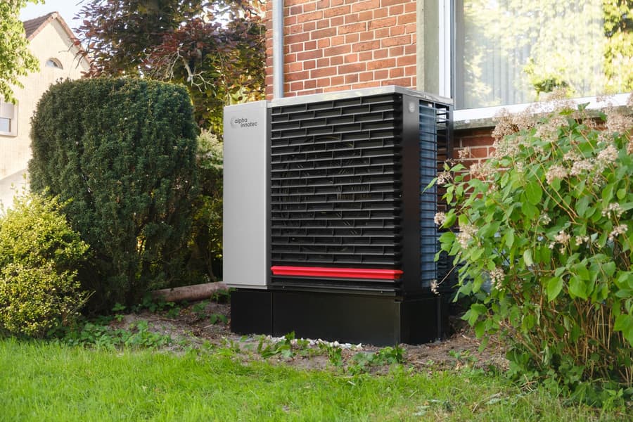 Heat pump outdoor unit on a garden lawn beside a brick house