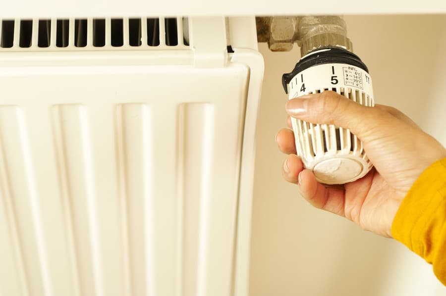 Hand turning the thermostatic valve on a white panel radiator