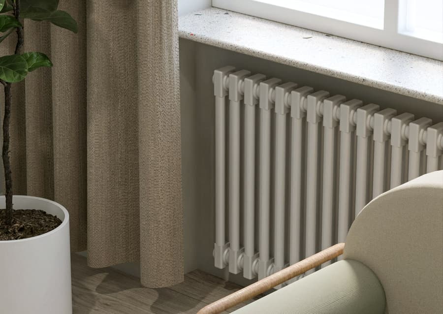 Panel radiator under a tall window in a finished living room, with a sofa and a plant beside it
