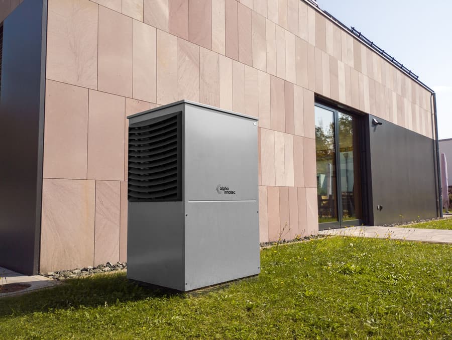 Outdoor heat pump unit on a lawn beside a modern house